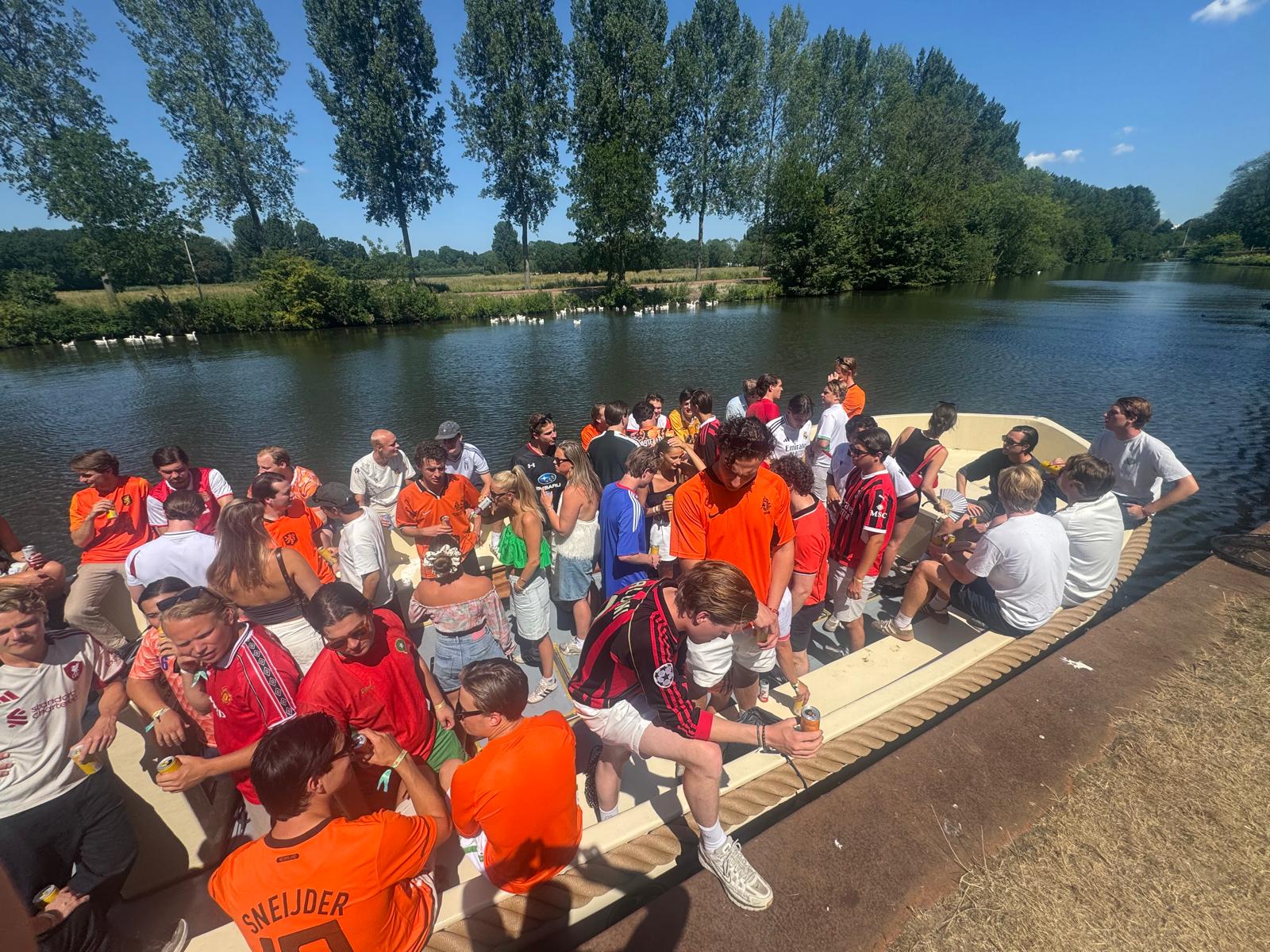 Grote groep feestvierders in oranje aan boord van een sloep tijdens Koningsdag